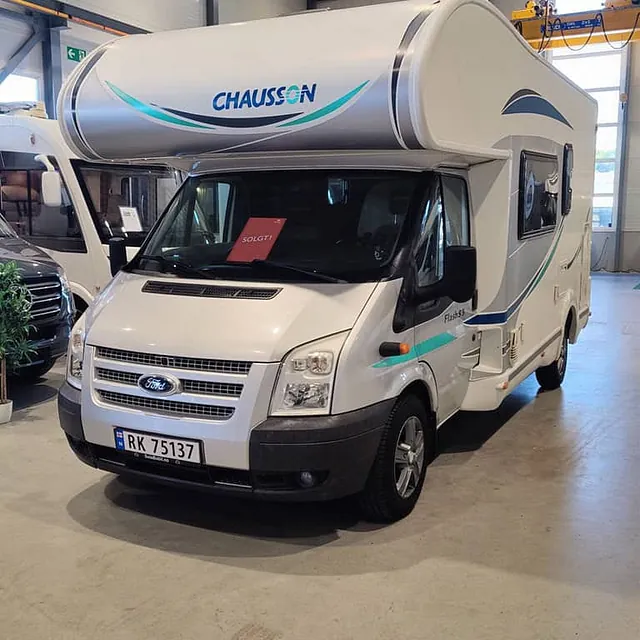 Hvit Chausson-bobil med registreringsnummer og "SOLGT"-skilt, parkert i hall med kran.