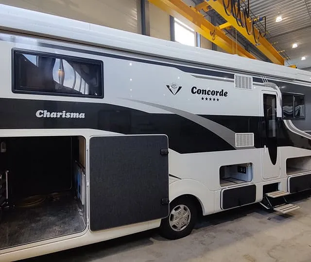 Stor Concorde Charisma-bobil med oppbevaringsrom åpent, vist innendørs i salgshall.