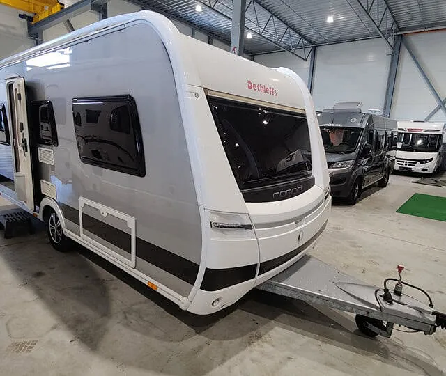 Moderne campingvogn av merket Dethleffs vist i stor hall med bobiler parkert rundt.