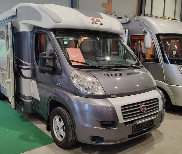 Sølvfarget Adria-bobil med åpen dør og "SOLGT"-skilt, parkert ved siden av en Hymer.
